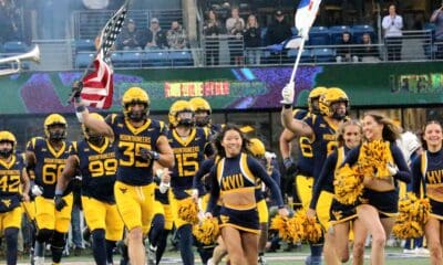 WVU Football team with US and WV flag and cheerleaders