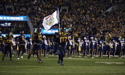 WVU Football running on field with West Virginia flag