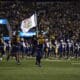 WVU Football running on field with West Virginia flag