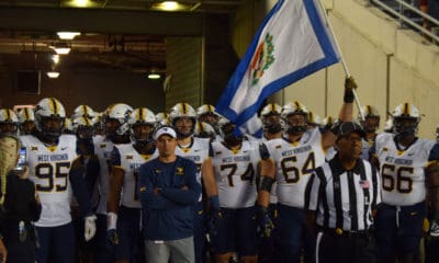 WVU Football HC Neal Brown with OL and Wyatt Milan carrying flag