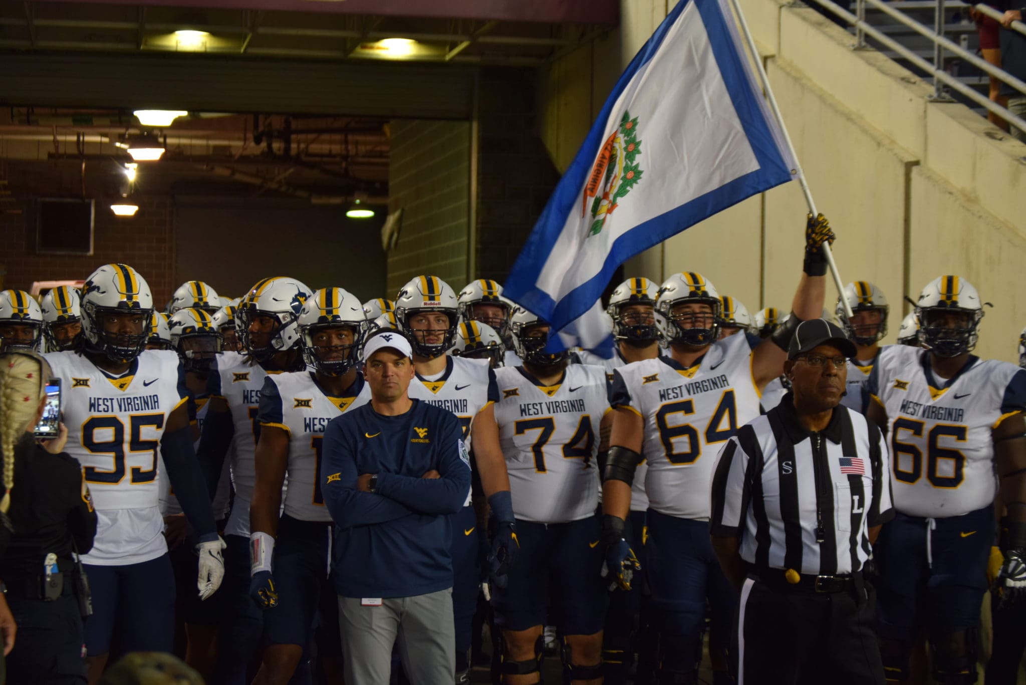 WVU Football HC Neal Brown with OL and Wyatt Milan carrying flag