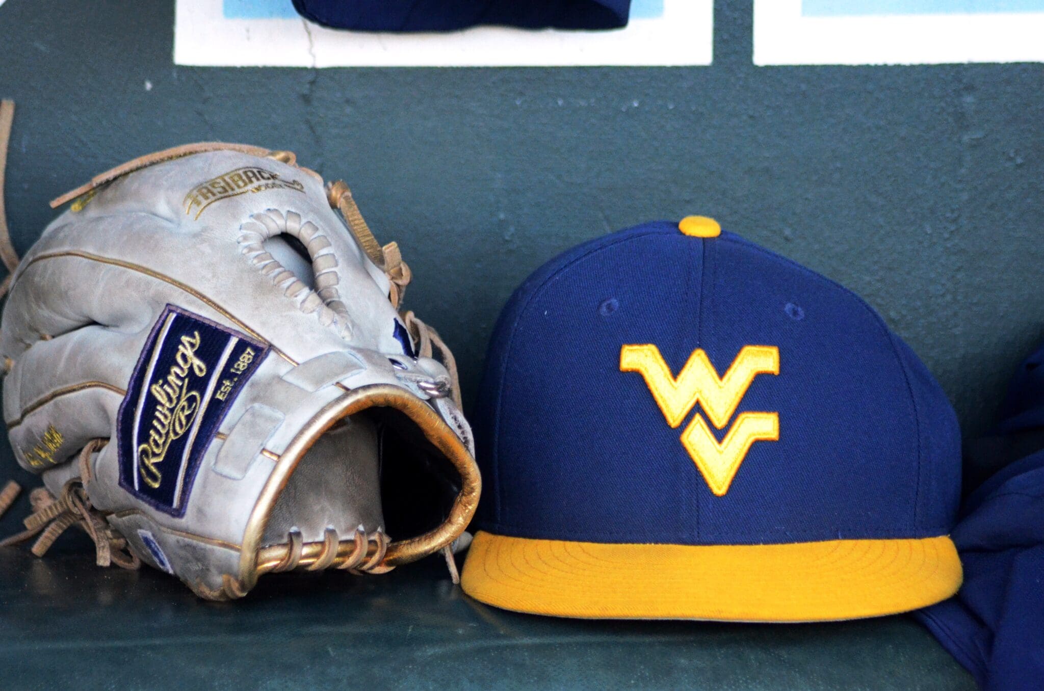 A WVU baseball hat and glove sits in the dugout as the Mountaineers played against North Carolina on June 8, 2024, in the Super Regionals of the NCAA Tournament at Boshamer Stadium in Chapel Hill, N.C. (Mitchell Northam / WV Sports Now)
